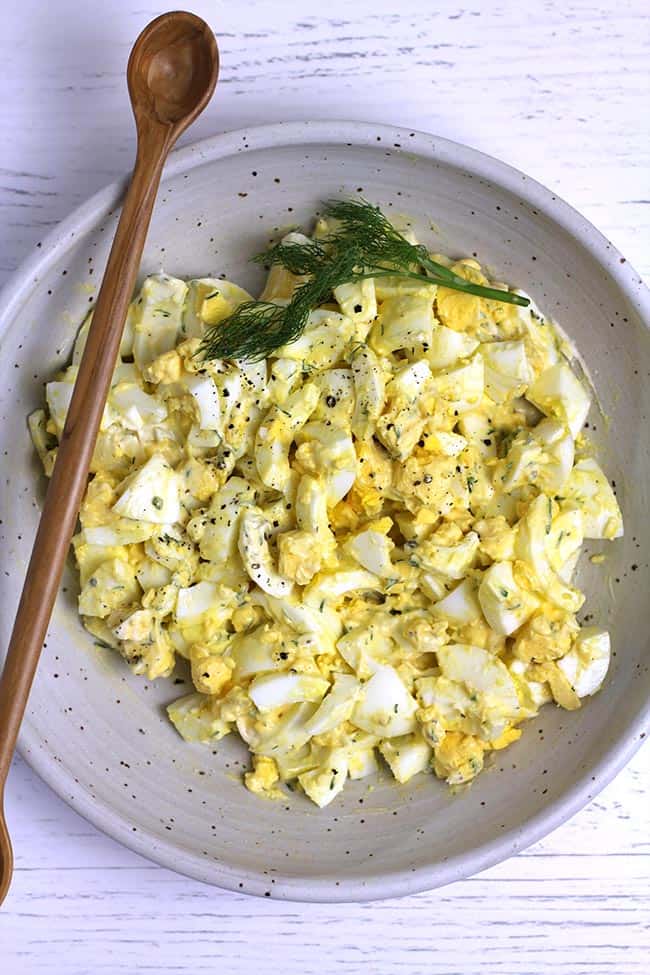 A bowl of class egg salad, after mixing, with a wooden spoon.