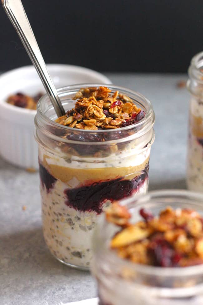 Close up of a jar of overnight oats, with a spoon, and granola on top.