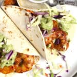 Overhead closeup shot of two grilled shrimp tacos with creamy avocado dressing and slaw.