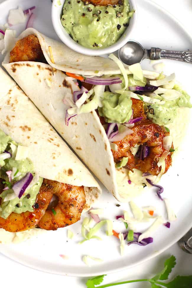 Overhead closeup shot of two grilled shrimp tacos with creamy avocado dressing and slaw.