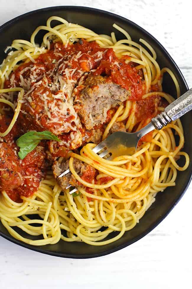 Closeup of a black bowl of homemade spaghetti and meatballs, with a fork twirling noodles.