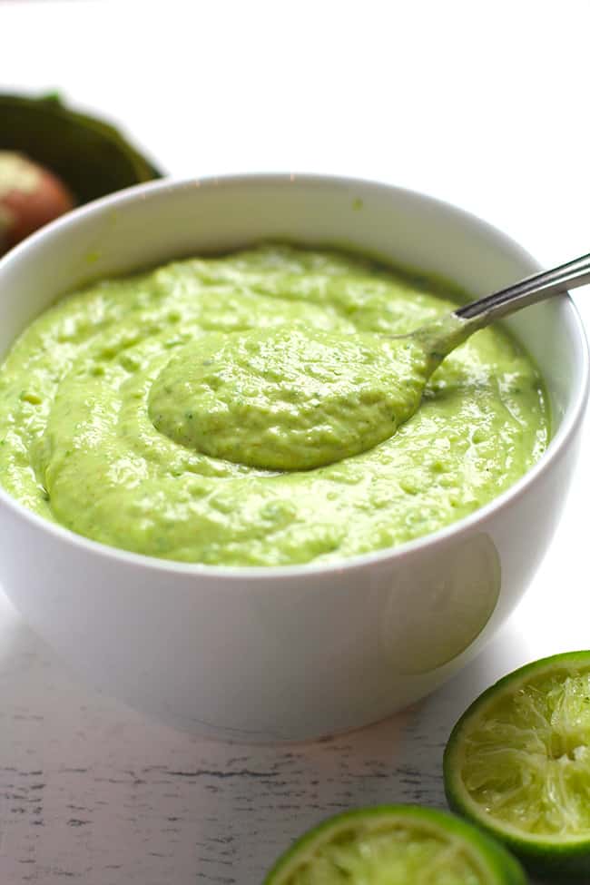 Side shot of some creamy avocado dressing, with a spoon inside.