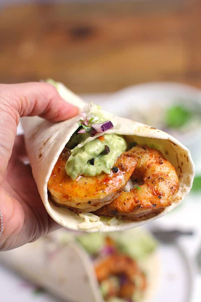 My hand holding a grilled shrimp taco, with creamy avocado dressing.