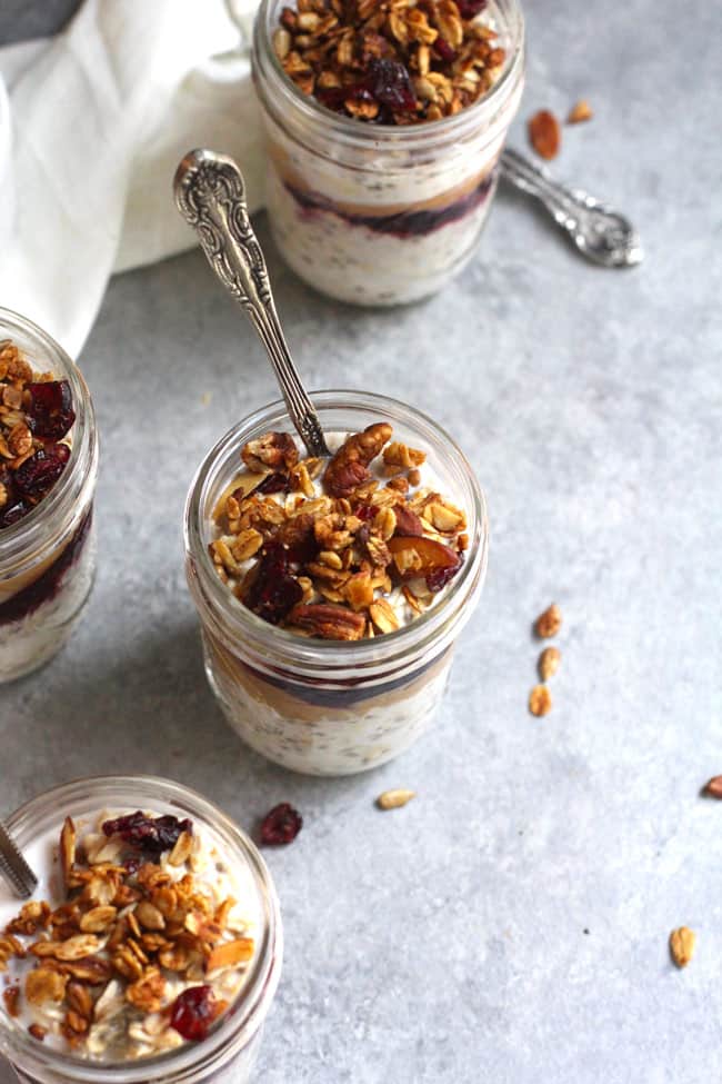 Overhead shot of four jars of peanut butter and jelly overnight oats, with spoons, and granola on top.