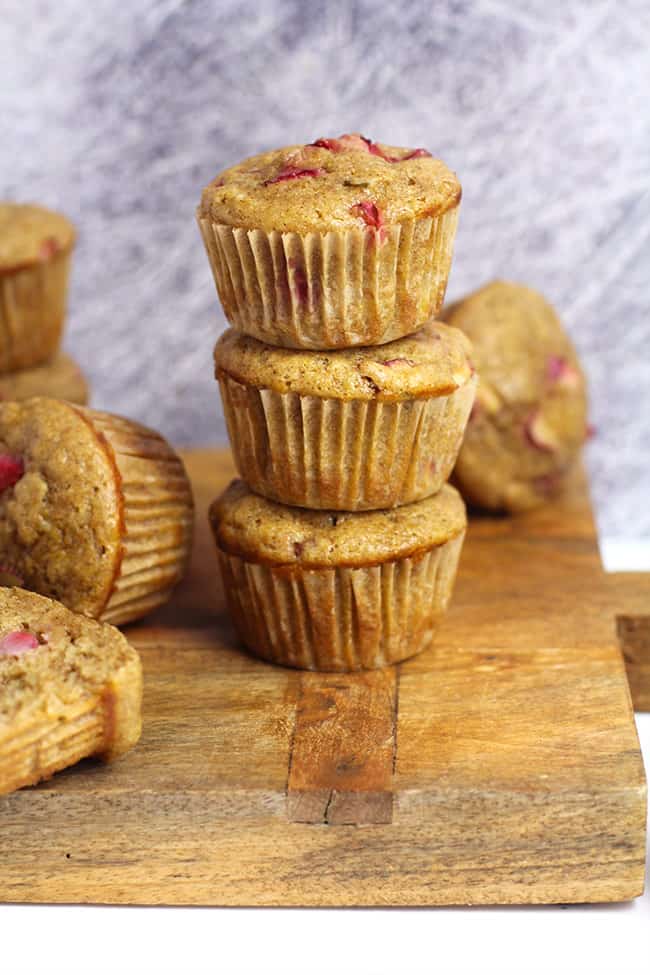 Three stacked strawberry rhubarb muffins on a wooden board.
