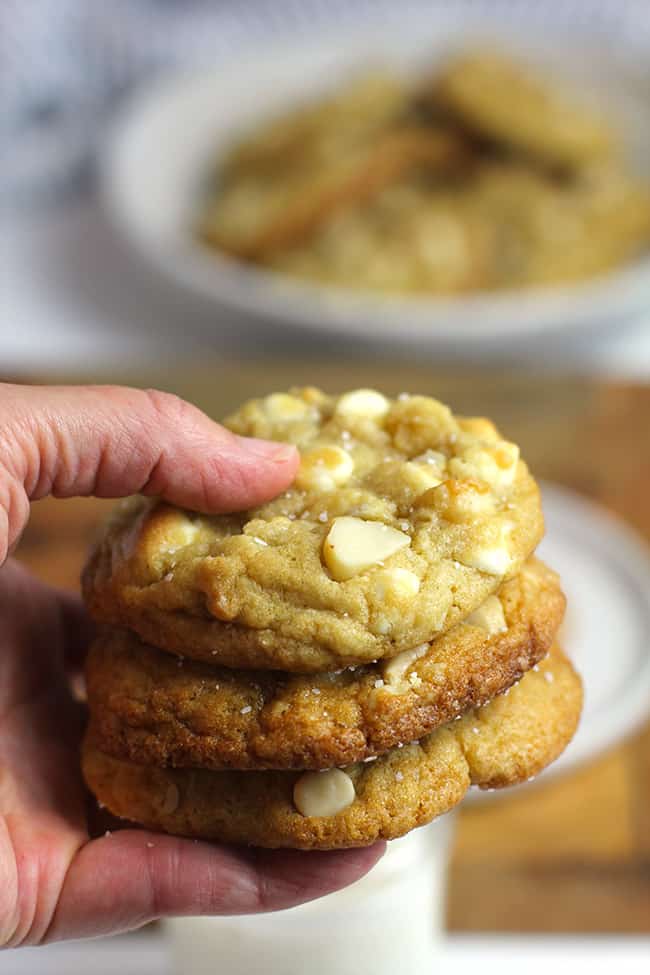 My hand holding a stack of three white chocolate macadamia nut cookies.