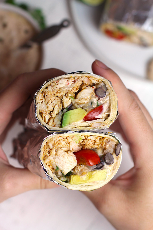 Two hands holding two Mexican chicken burritos, showing the insides of the burritos.