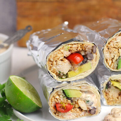 Side view of Mexican Chicken Burritos, wrapped in foil, on a white plate.