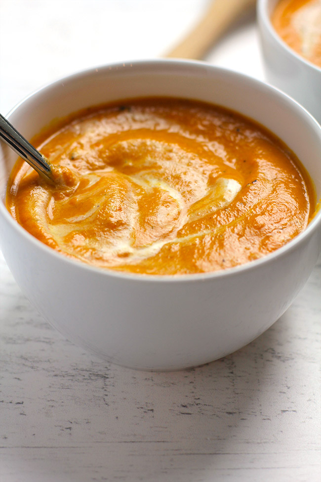 Side view of a white round bowl of carrot soup, with cream swirled in.