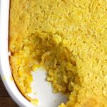Close up shot of a portion of a creamy corn casserole, with a scoop missing.