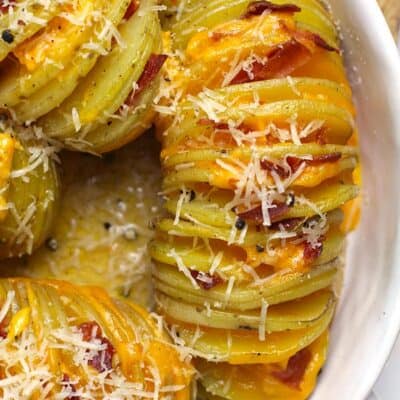 Close up of some cheesy hasselback potatoes, in a white baking dish.