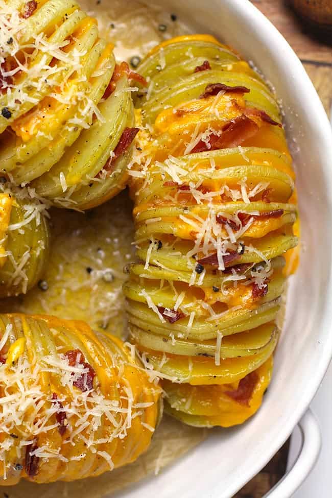 Close up of some cheesy hasselback potatoes, in a white baking dish.