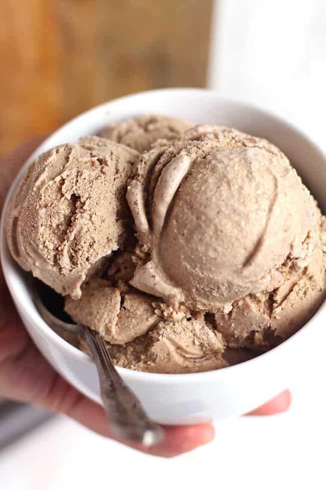 A hand holding a round white bowl of double chocolate ice cream.