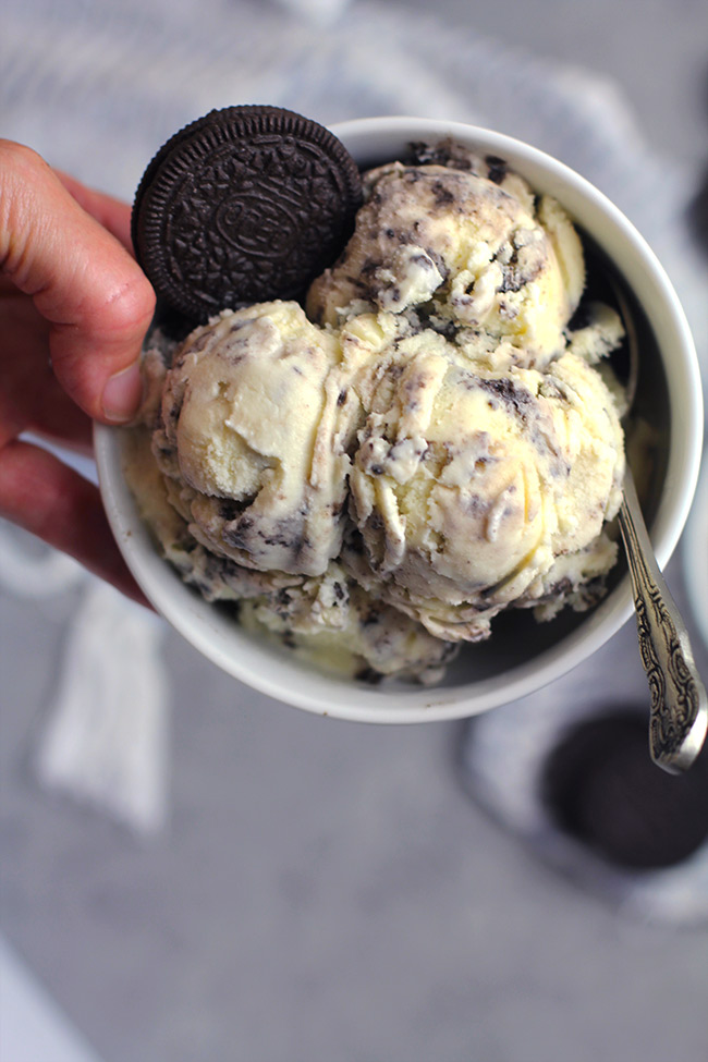 A hand holding a round white bowl of cookies and cream ice cream.