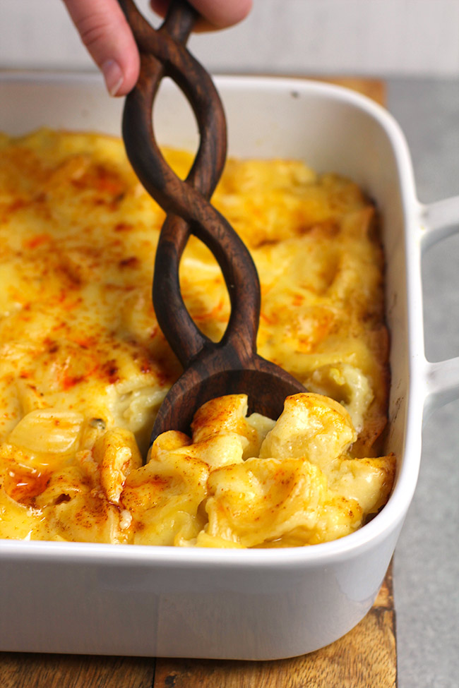 A hand using a wooden spoon to scoop our some quick and easy Mac and cheese.