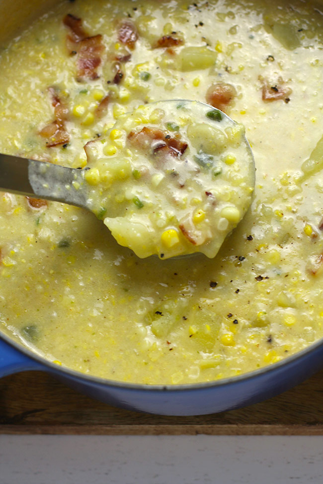 A stock pot of corn chowder with a soup ladle pulling upward.
