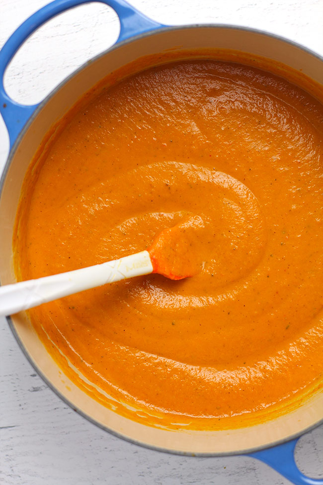 A blue stock pot with creamy carrot soup inside.