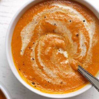 Closeup shot of a white bowl of carrot soup with cream swirled on top.