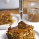 A fork in a piece of apple cake with caramel sauce.