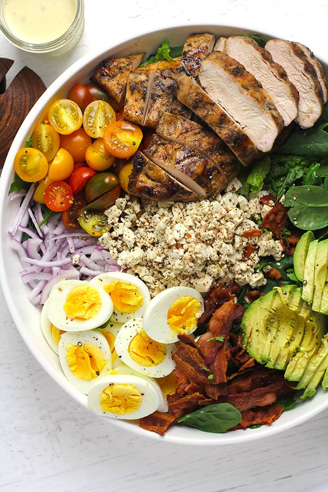 A large serving bowl full of ingredients for grilled chicken Cobb salad.