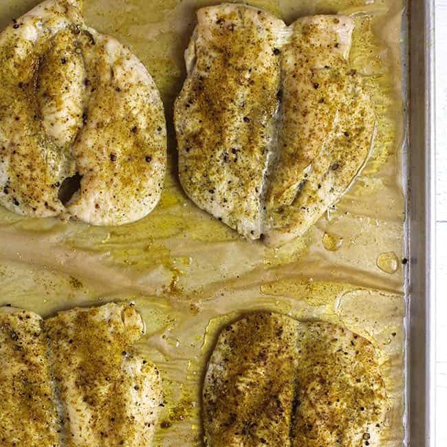 Overhead shot of four baked butterflied chicken breasts, with curry powder.