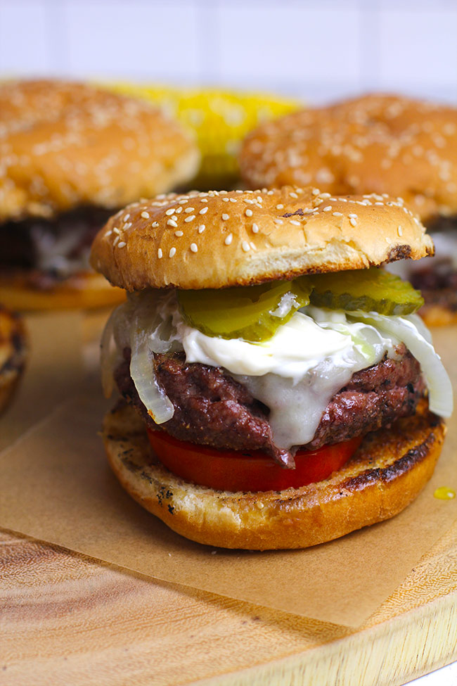 Side shot of a platter of four grilled juicy Lucy burgers, with a closeup on one burger.