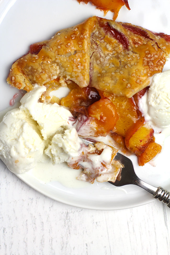 Closeup of a fork on a plate of peach galette and vanilla ice cream.