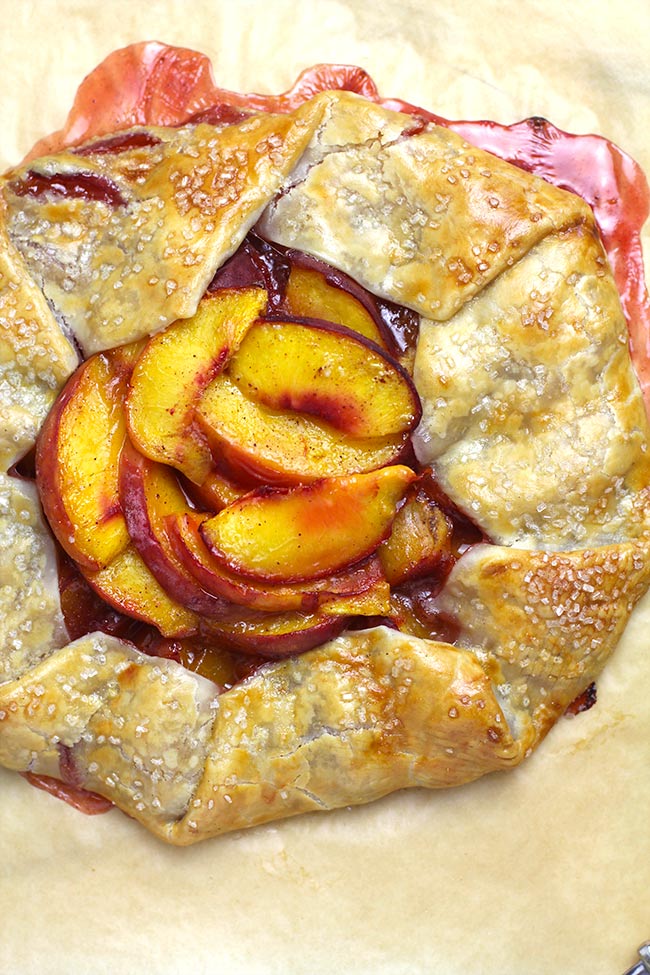 Overhead shot of a peach galette on tan parchment paper.