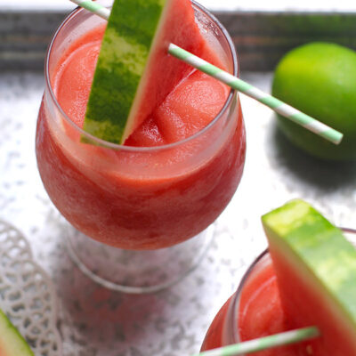 Two glasses of watermelon frose, on a gray tray with watermelon wedges for garnish.