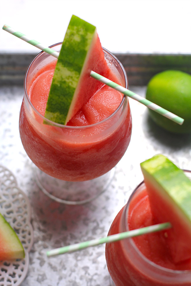 Two glasses of watermelon frose, on a gray tray with watermelon wedges for garnish.