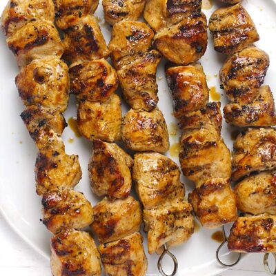 A white plate with five chicken skewers.