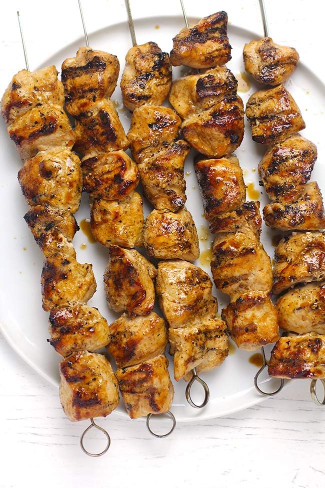 A white plate with five grilled chicken skewers.