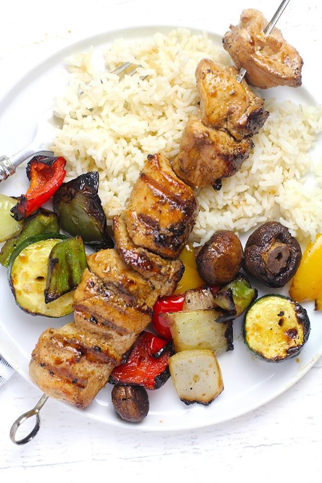 A plate of rice, veggies, with one chicken skewer on top.
