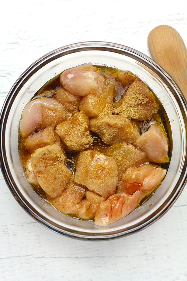 A glass bowl of chicken chunks with marinade ingredients.