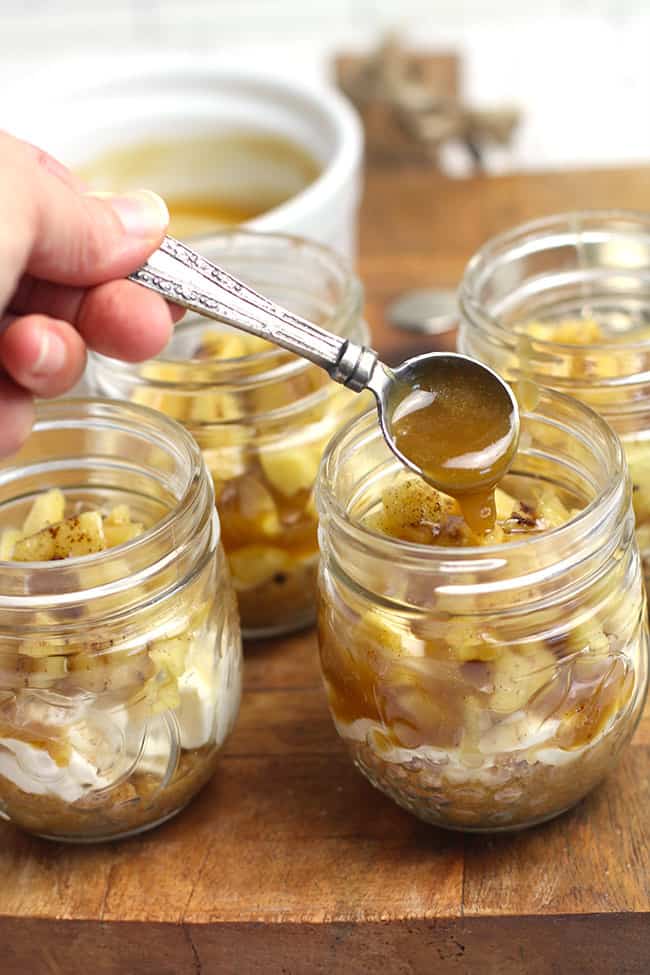 A hand drizzling some caramel sauce in the mason jars with the apple cheesecakes.