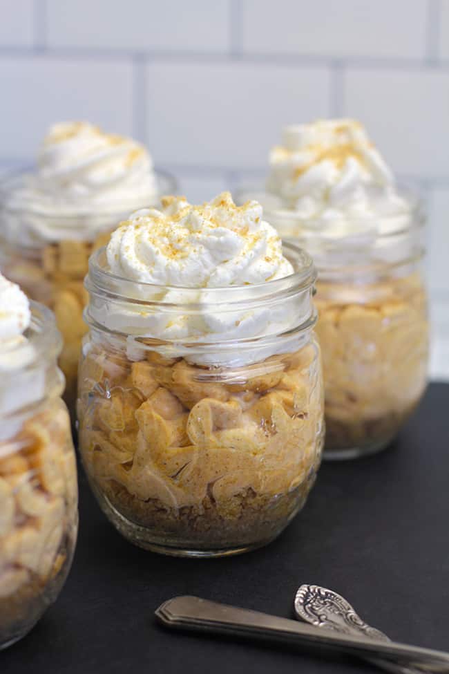 Side shot of four mini jars of pumpkin cheesecake, on a black board.