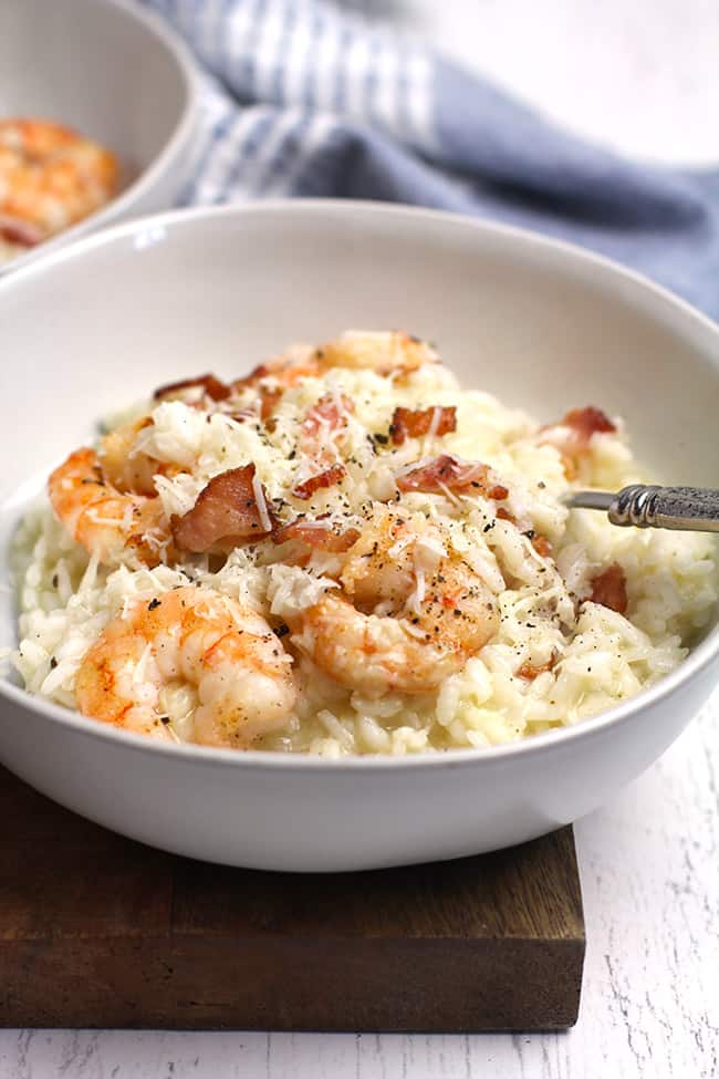 Side shot of a white bowl of creamy shrimp risotto with bacon.