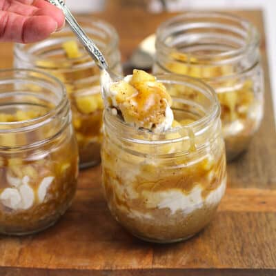 Side shot of a hand spooning out a bite of caramel apple cheesecake, in a mason jar.
