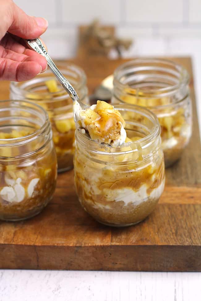 Side shot of a hand spooning out a bite of caramel apple cheesecake, in a mason jar.