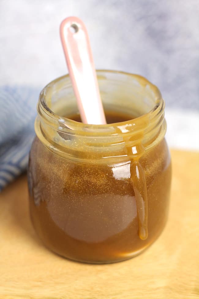 A mason jar with caramel sauce, with a drizzle of sauce on the side of the jar.