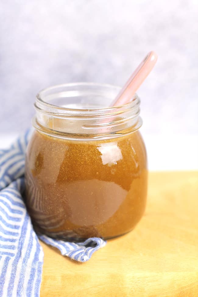 Side shot of a mason jar filled with 5-ingredient caramel sauce, with a pink spoon inside.