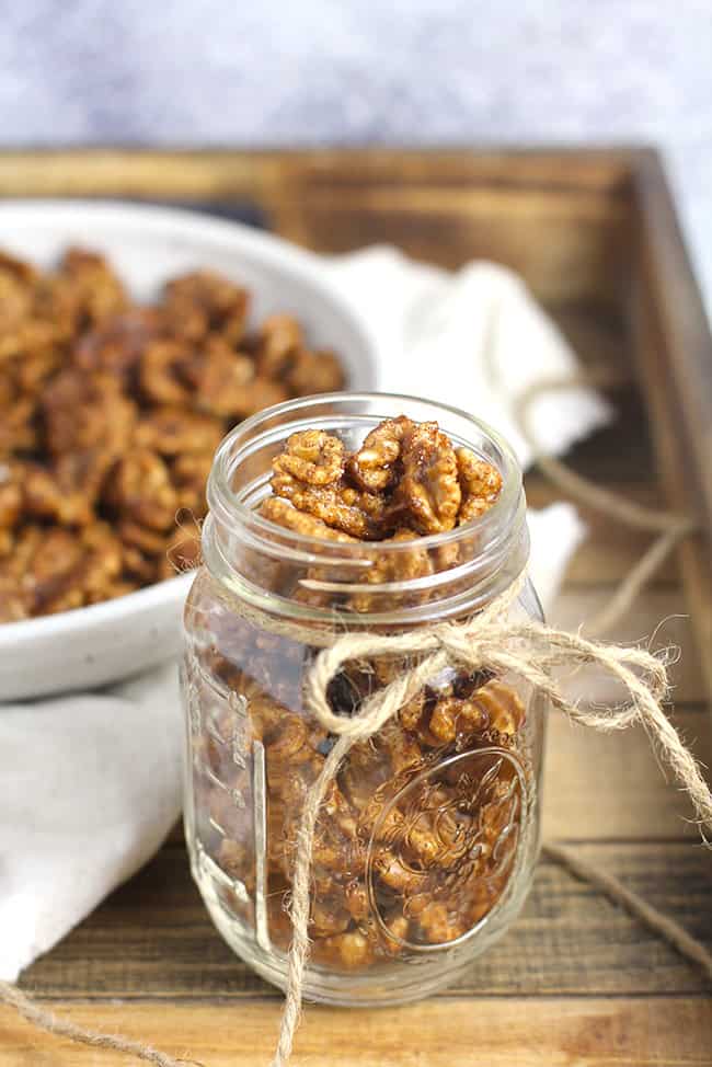 A jar of candied walnuts with a bowl in the background.