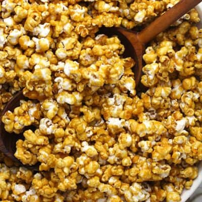 A large white bowl of caramel popcorn, with some wooden spoons.