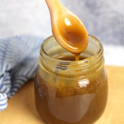 A spoon drizzling caramel sauce into a mason jar.