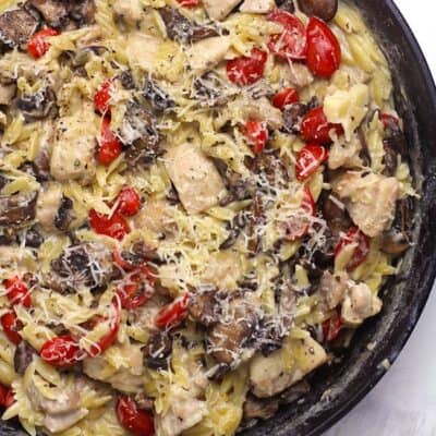 Overhead shot of a parmesan chicken orzo skillet, with mushrooms and tomatoes.