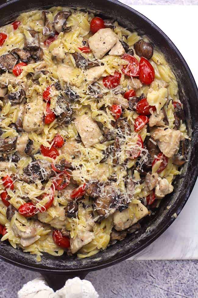 Overhead view of a parmesan chicken orzo skillet, with mushrooms and tomatoes.