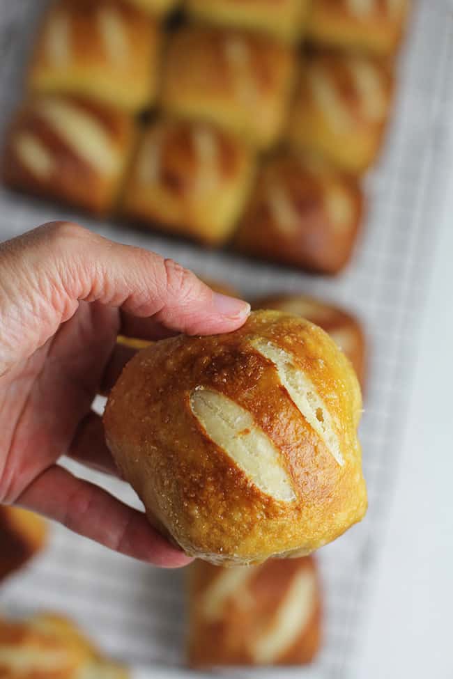 A hand holding a homemade pretzel roll, with others in the background.