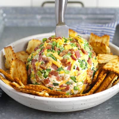 Side view of a jalapeño popper cheese ball with crackers, on a shallow bowl.