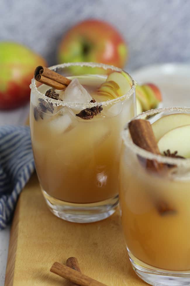 Two glasses of apple cider margaritas with cinnamon sticks and apple slices.