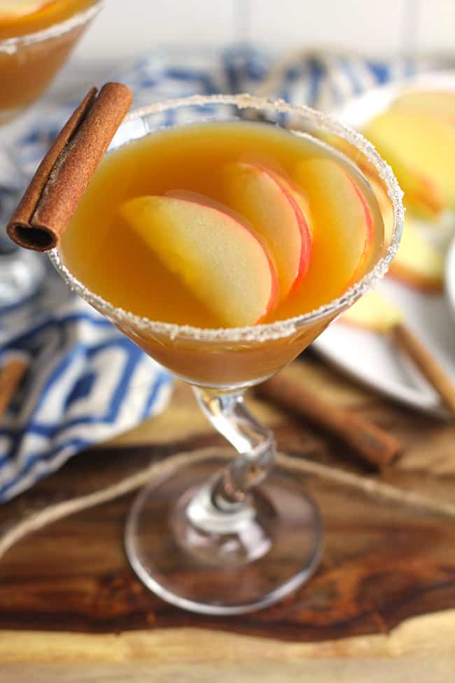 Side overhead shot of a apple cider martini, with apple slices inside and a cinnamon stick.